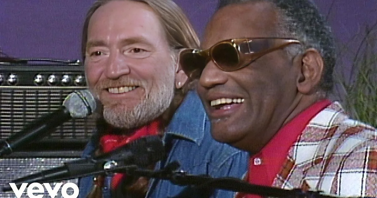 Two smiling men, one with a beard, stand together in front of microphones, wearing casual attire.