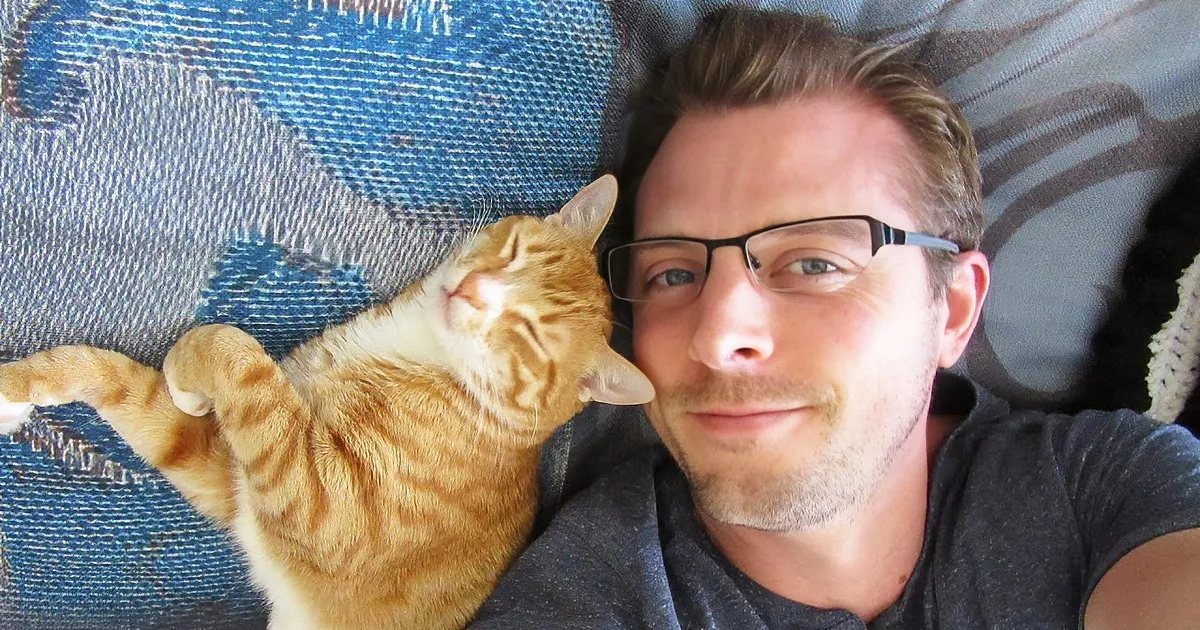 A man and his orange tabby cat are lying together on a blue patterned blanket.