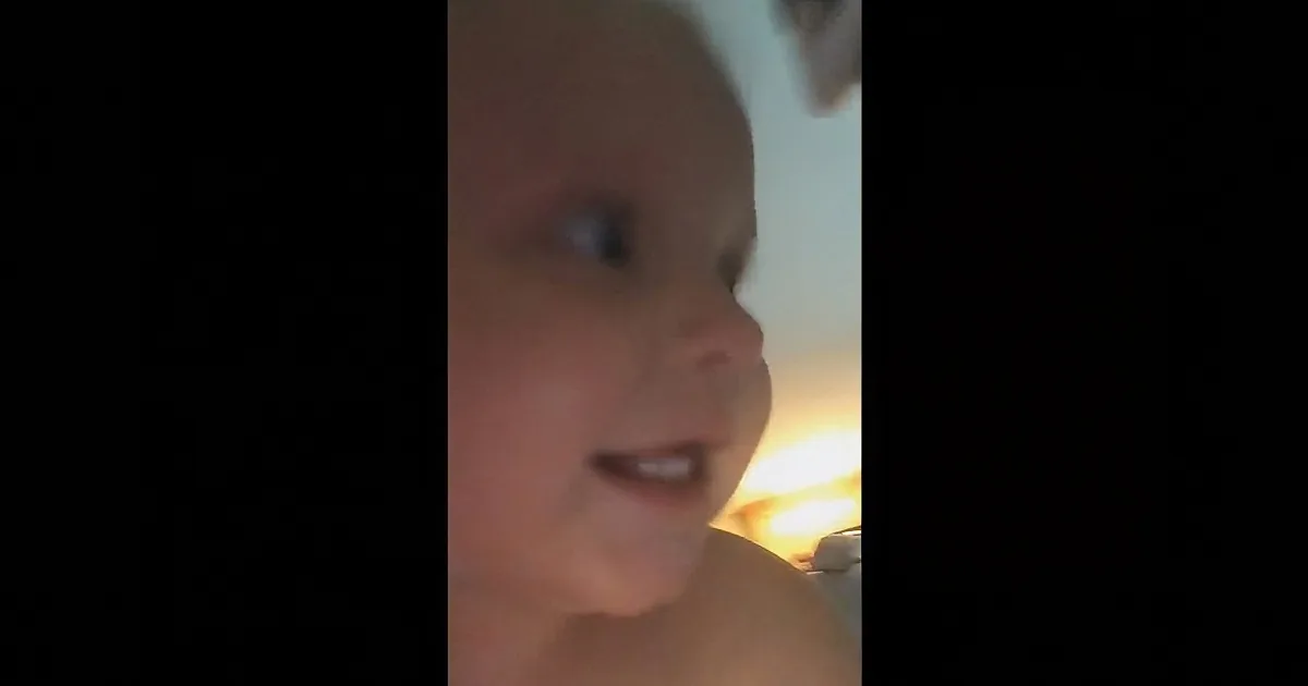 A baby is looking to the side with a curious expression, mouth slightly open.