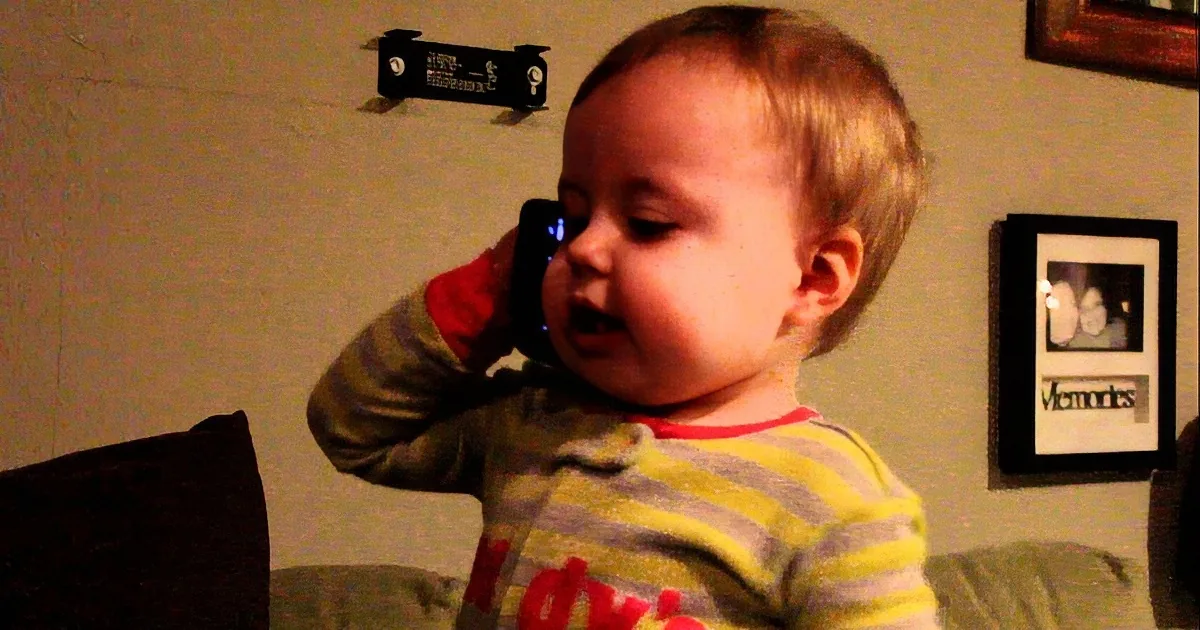 A toddler in striped pajamas is holding a phone to their ear, appearing to talk.