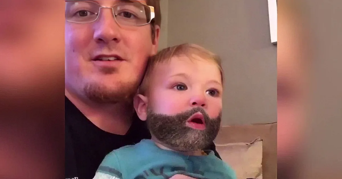 A man holds a child with a beard filter, both looking surprised.