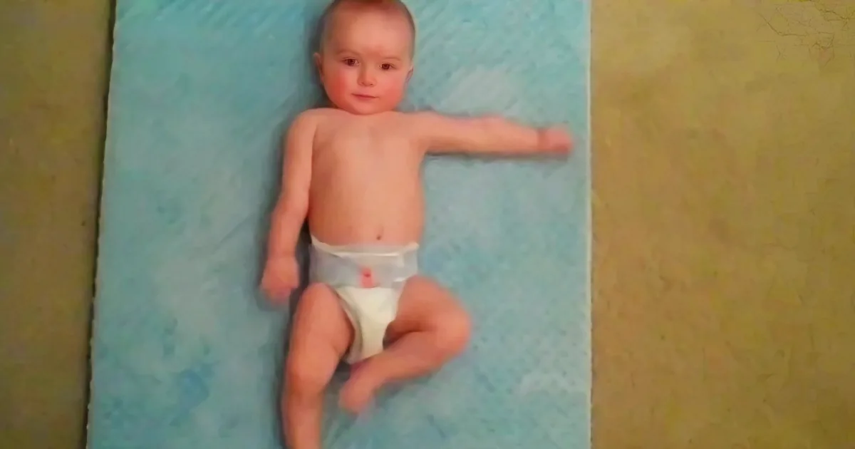 A baby in a diaper lies on a blue mat, arms outstretched, looking up.