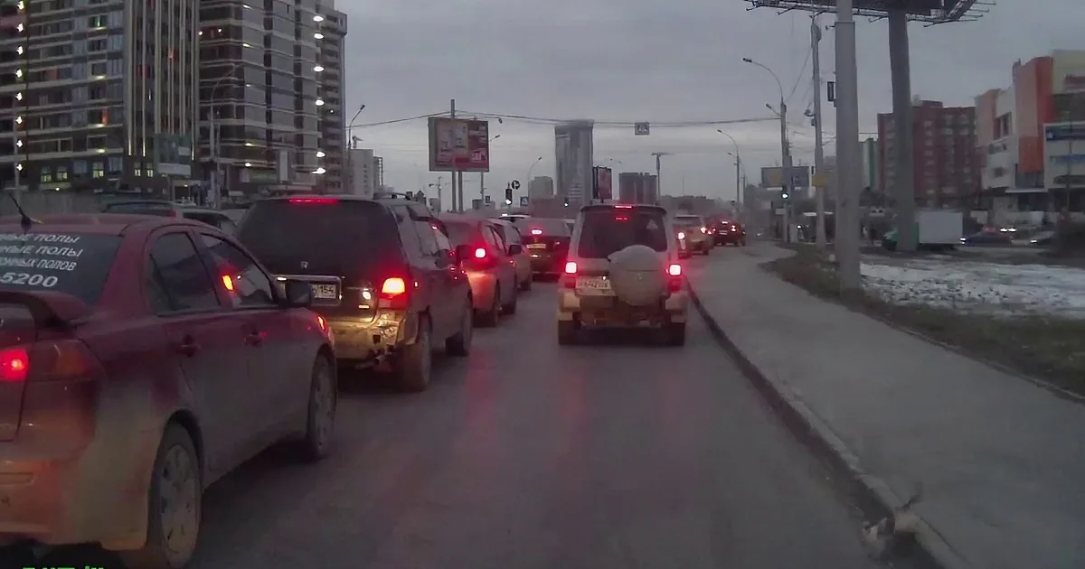 Cars with red brake lights are stopped in traffic on a city street at dusk.