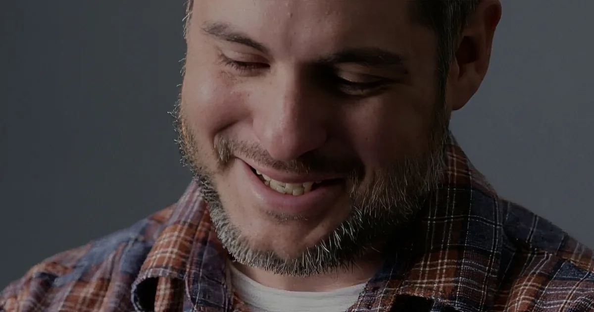 A man with a beard and plaid shirt is smiling with his eyes closed.