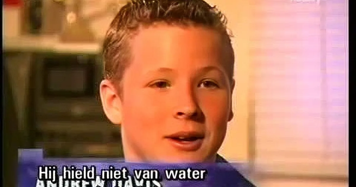 A young boy with short hair, wearing a light-colored shirt, is speaking in front of a blurred background.