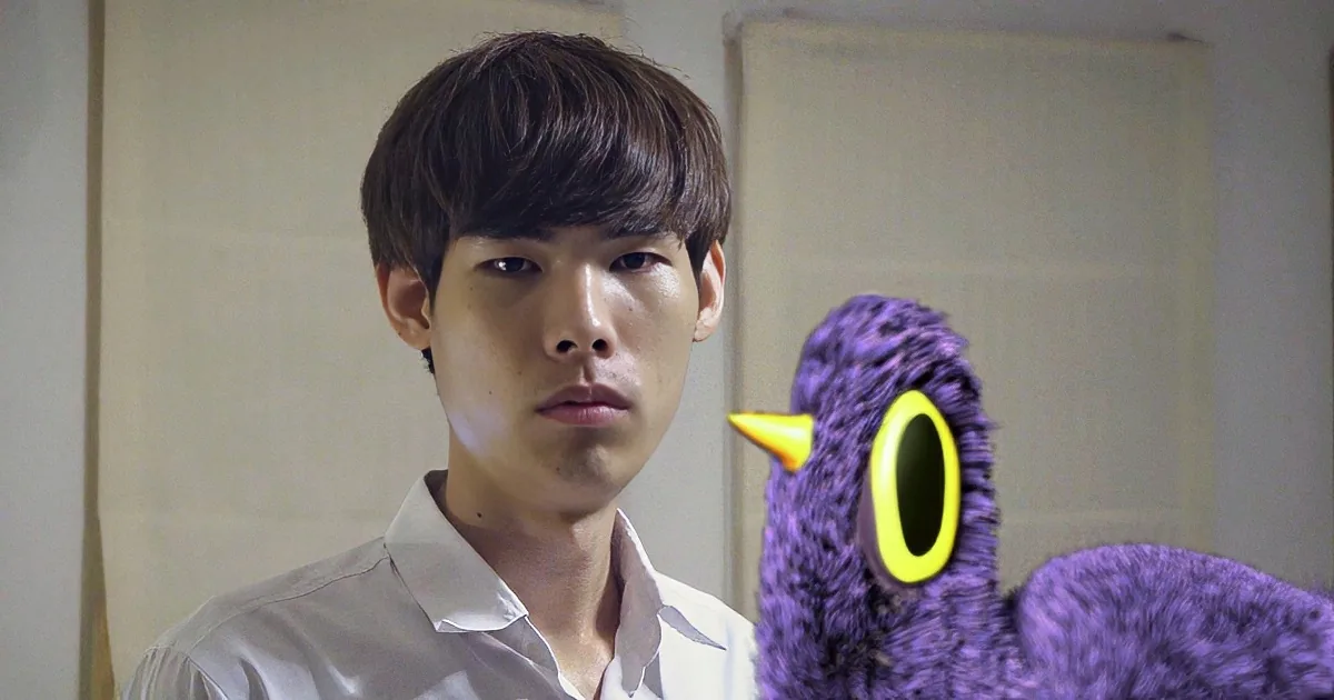 A person in a white shirt stands next to a purple puppet with yellow eyes in a room.