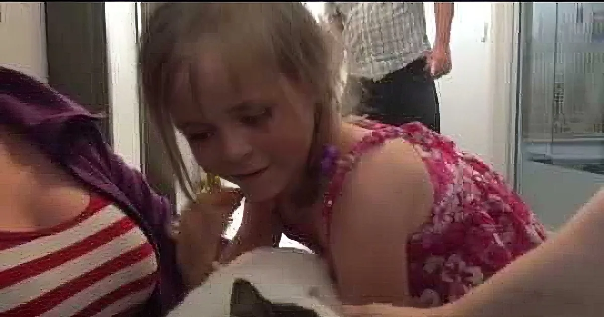 A young girl in a pink dress is holding a white cat, looking down at it with a smile.