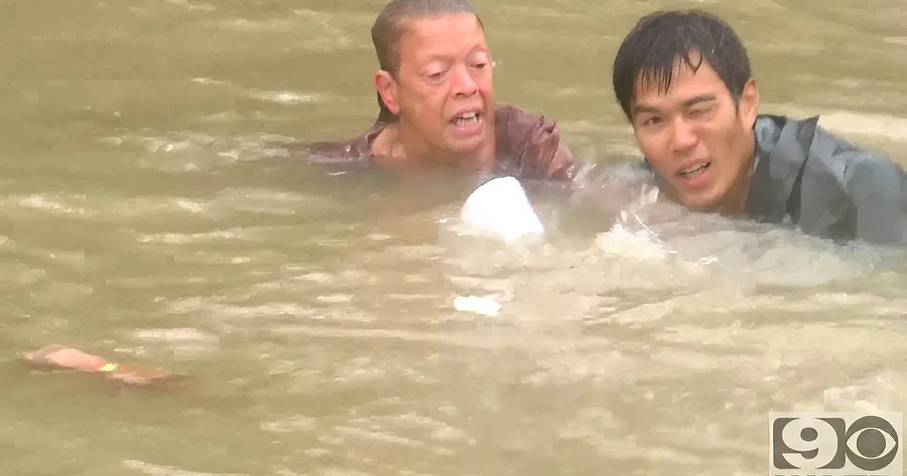 Two individuals are struggling in floodwaters, with one person appearing to be in distress.