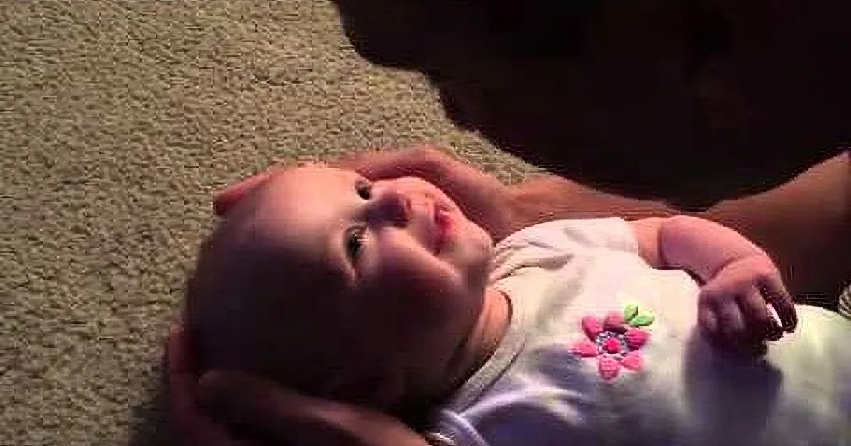 A baby lies on a carpet, looking up at a person holding their hands.