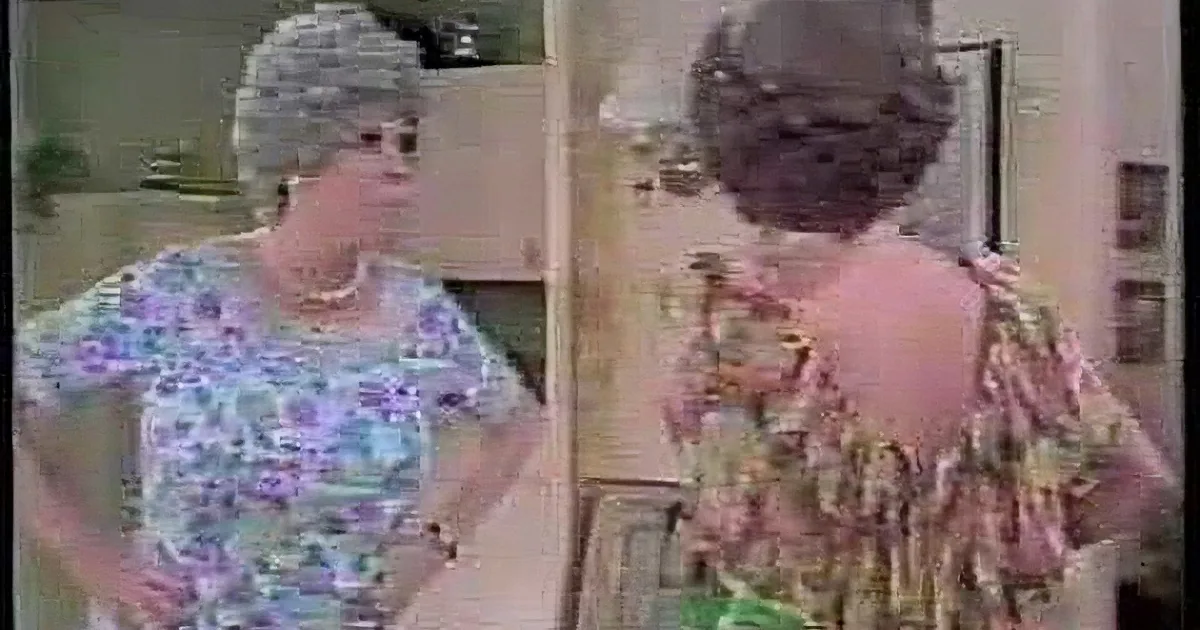 A woman in a floral dress stands with hands on hips, facing another woman in a similar dress who is turning away.