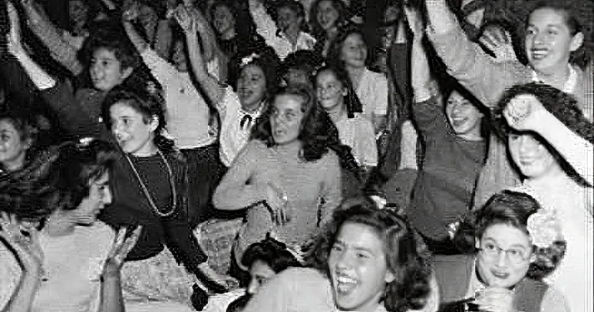 A group of women in a crowd, some raising their hands, smiling and enjoying themselves.