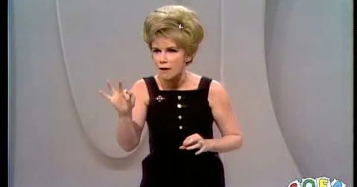 A woman in a black dress with a white background and a hand gesture.