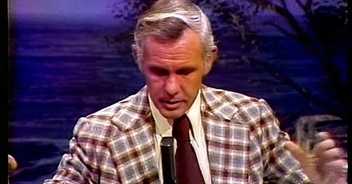 A man in a plaid suit and tie appears to be speaking or listening intently.