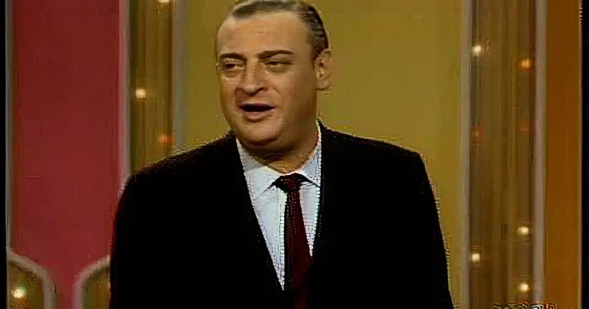 A man in a suit and tie is smiling, standing in front of a colorful, patterned background.