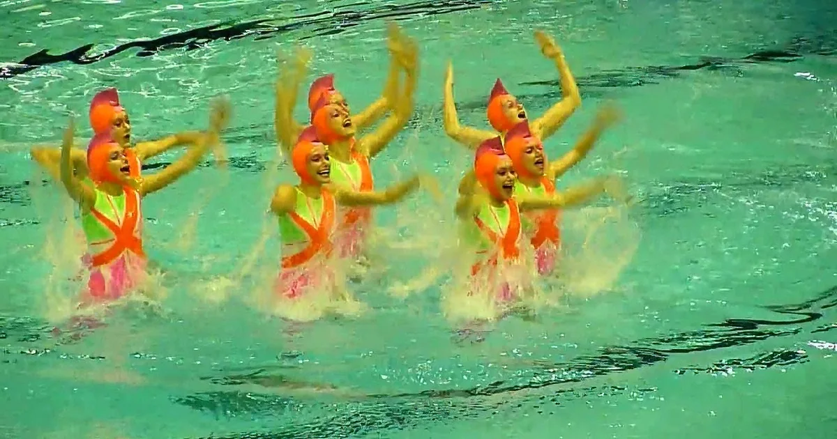 A synchronized swimming team in vibrant costumes performs a routine in a pool.