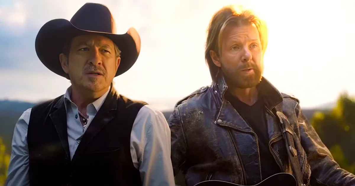 Two men, one in a cowboy hat and vest, the other in a leather jacket, stand outdoors with a scenic background.