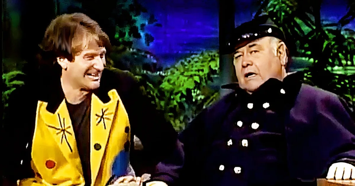 A man in a yellow jacket with a star design is smiling while another man in a dark uniform with white buttons looks on.