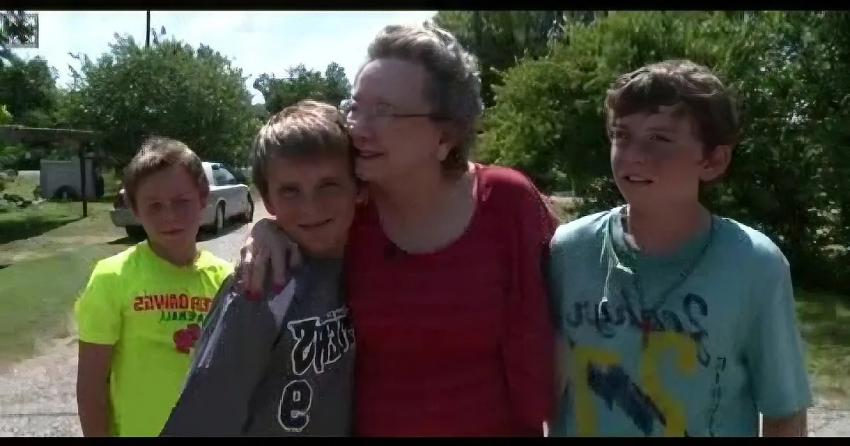 An elderly woman in red hugs a young boy, surrounded by three other children outdoors.