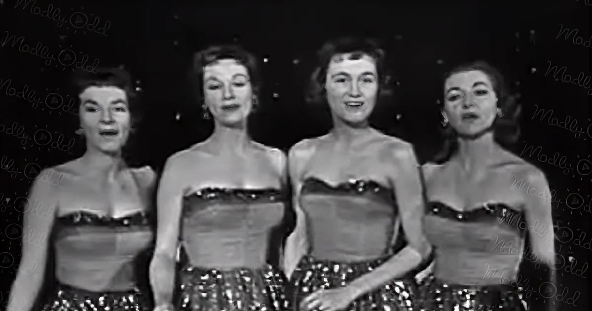 Four women in strapless dresses with sequined skirts perform together.