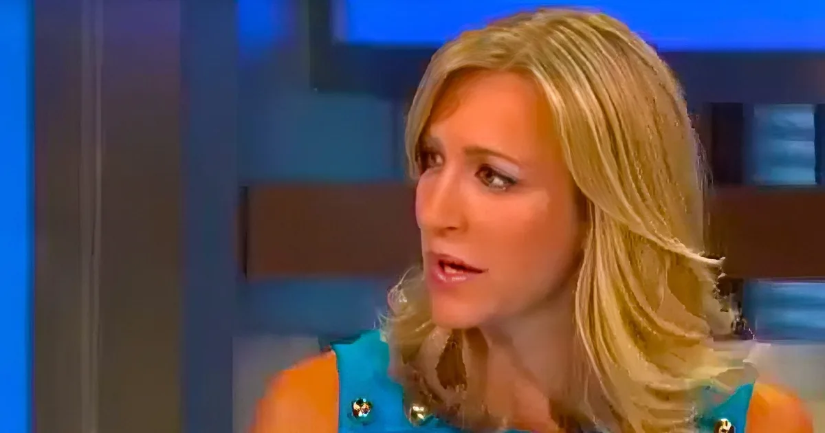 A woman with blonde hair in a blue dress is speaking on a television show.