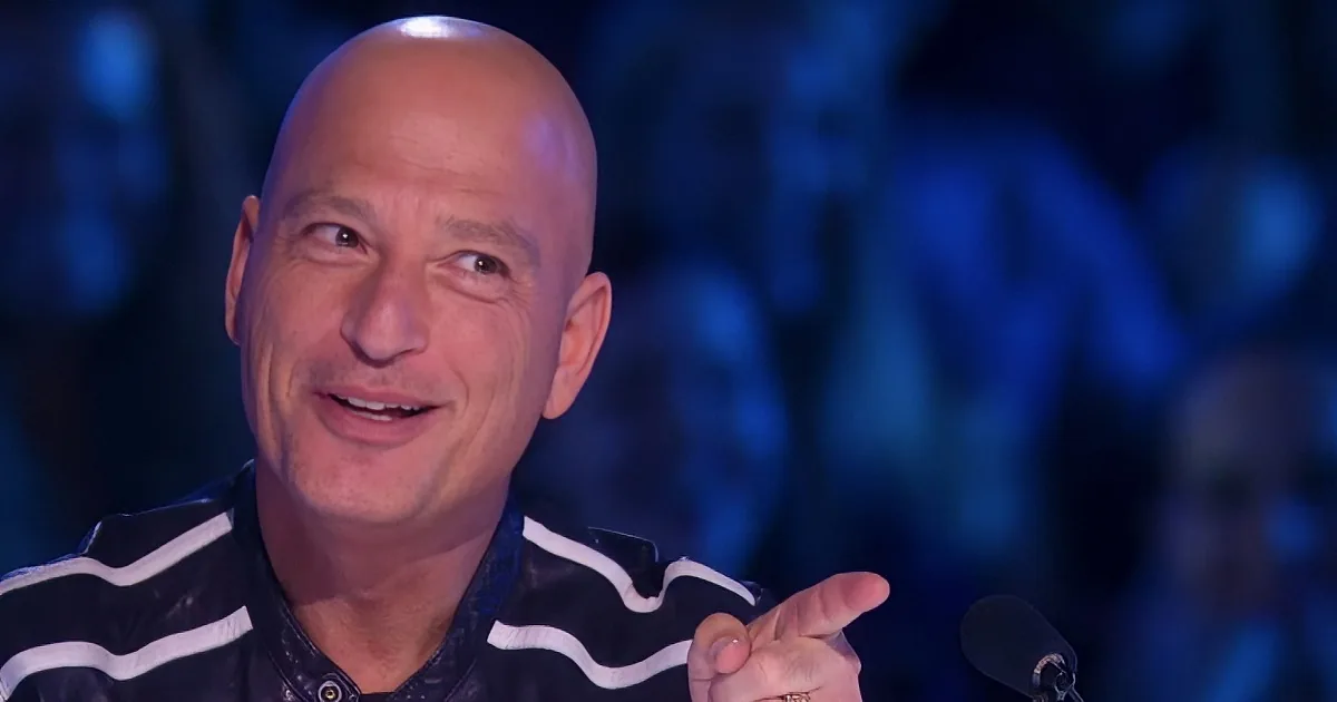 A bald man in a black and white striped shirt gestures with his right hand while speaking.
