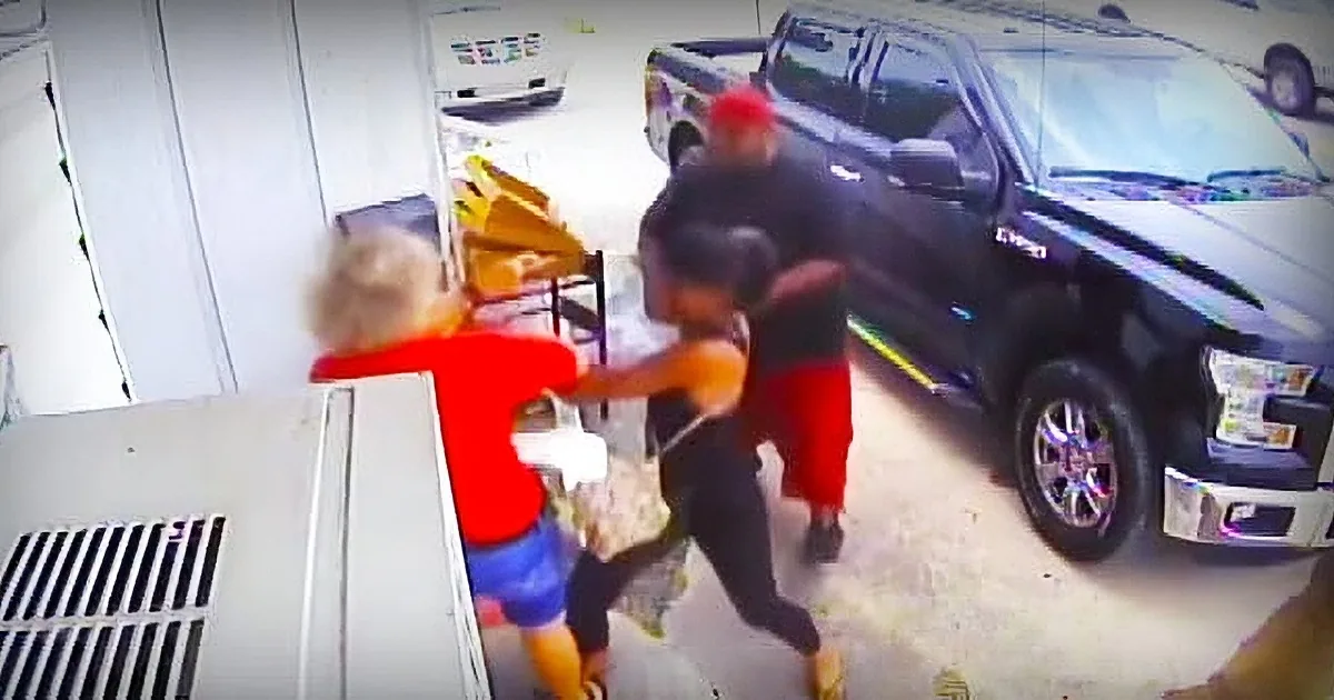 A person in a red shirt and black pants is being held by another person in a black shirt and red pants near a black truck.