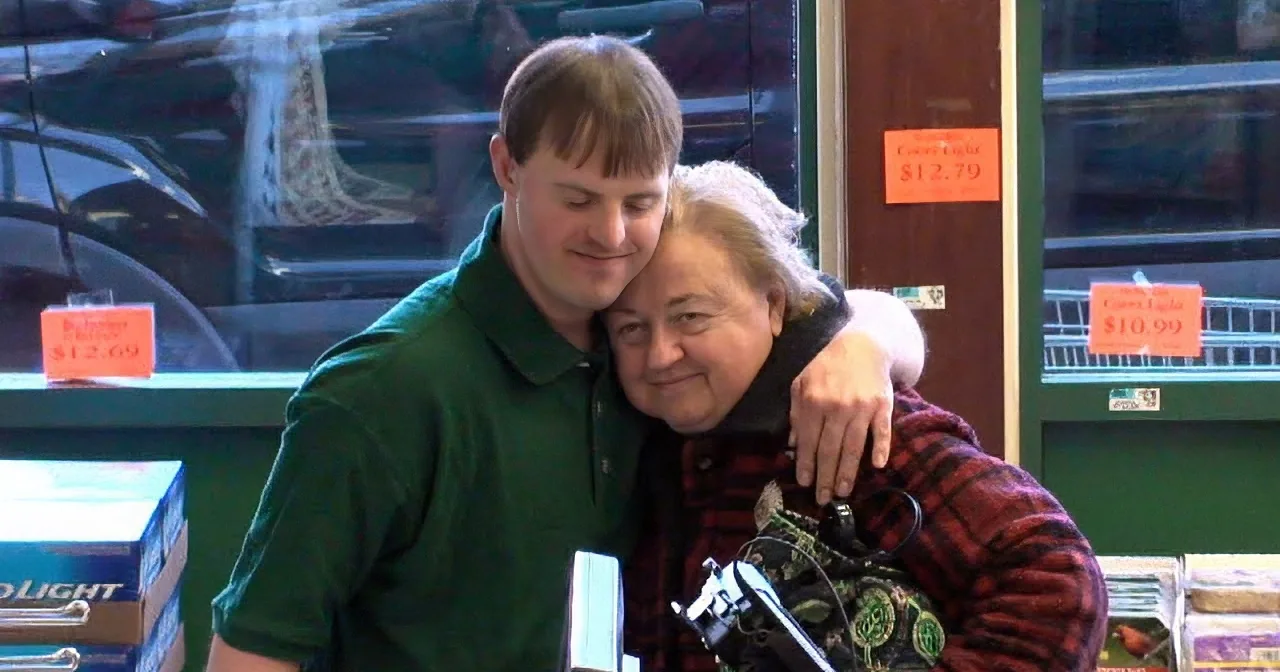 A man in a green shirt hugs an older woman in a store, with price signs visible in the background.