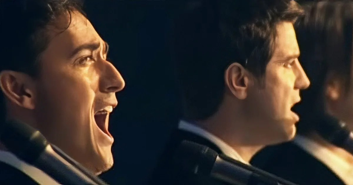 A man in a suit sings passionately into a microphone, his mouth wide open.