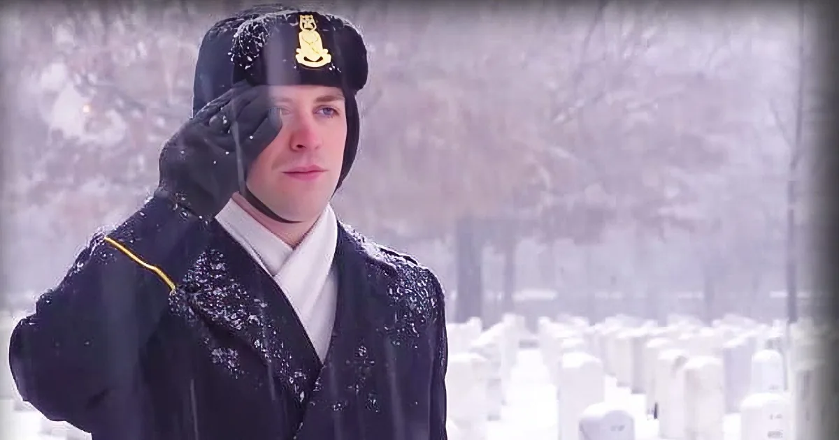 A person in a dark uniform salutes in a snowy cemetery.
