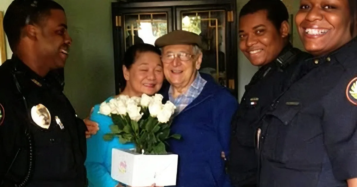 An elderly couple holds flowers and a card, flanked by two police officers, all smiling.