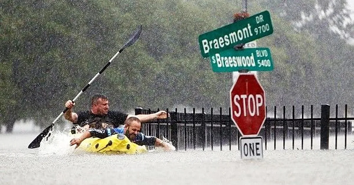 Two people paddle through floodwaters, navigating past Braesmont and Braeswood street signs.