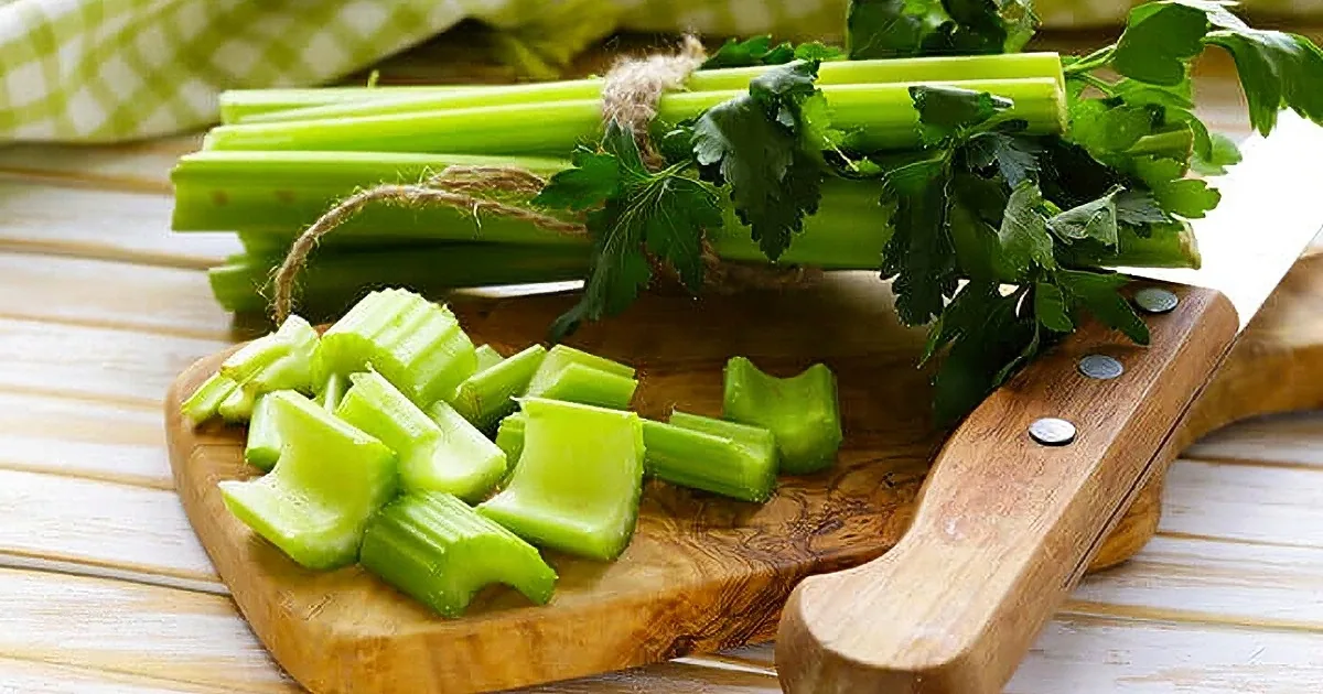 Celery stalks and chopped pieces on a wooden cutting board with a green checkered cloth in the background.