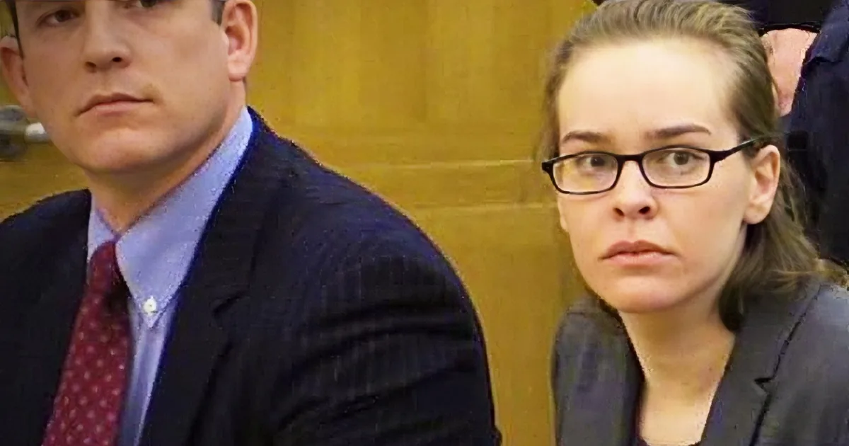 A man in a suit and tie sits next to a woman in glasses in a courtroom setting.