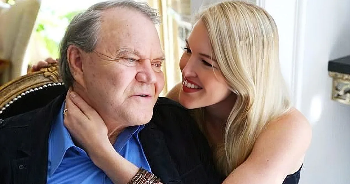 A woman embraces an older man, both smiling warmly, in a cozy indoor setting.