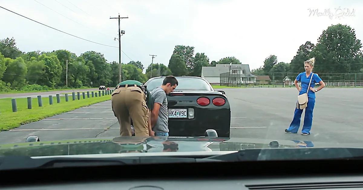 A man and woman stand near a black sports car in a parking lot, with a police officer inspecting the car.
