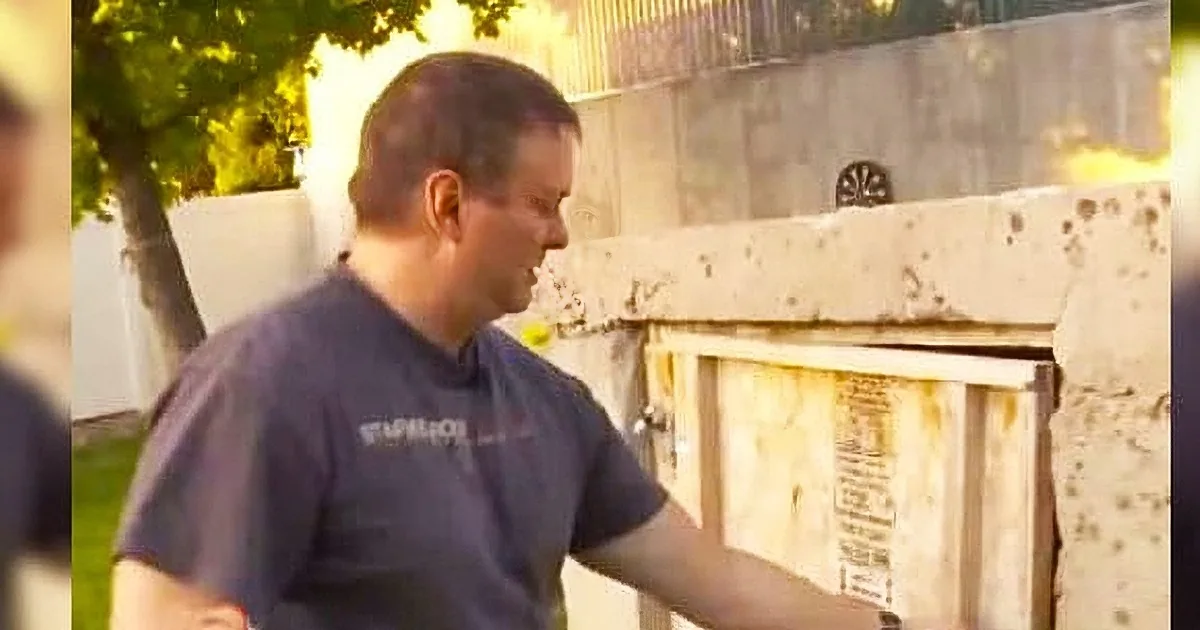 A man in a dark shirt is standing near a white fence, looking down.