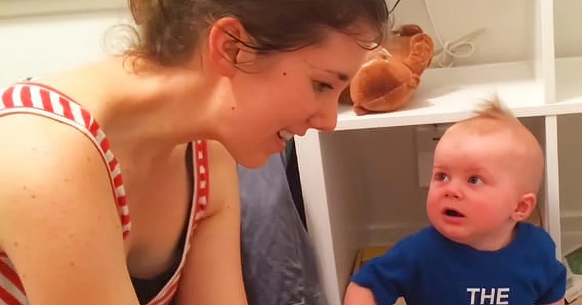 A woman in a red and white striped tank top leans close to a baby in a blue shirt, both looking at something off-camera.