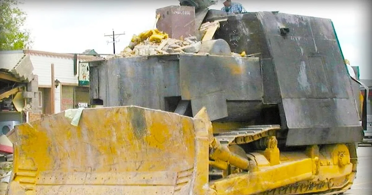 A large, yellow construction vehicle is parked next to a large, dark, armored vehicle in a debris-filled area.