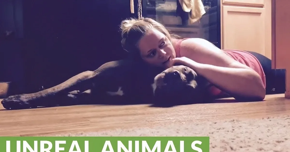 A woman lies on the floor with a dog, both resting on a wooden surface.