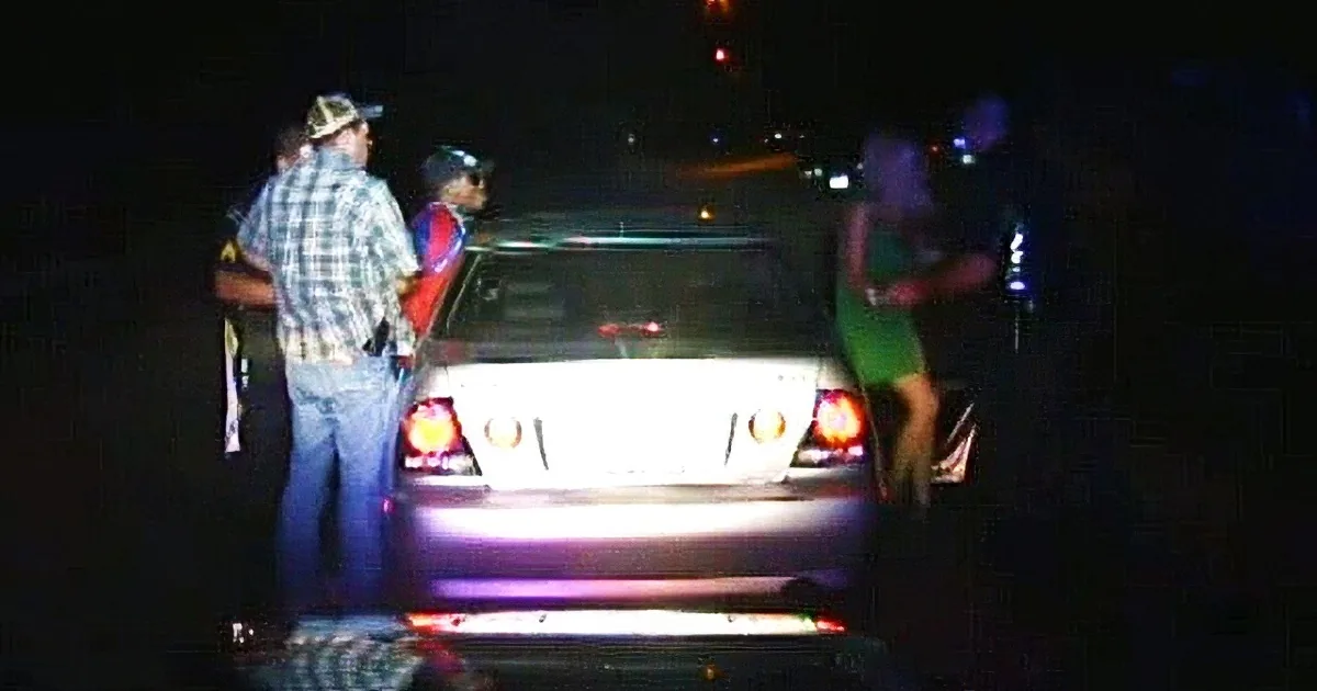 A police officer stands beside a car with flashing lights at night.