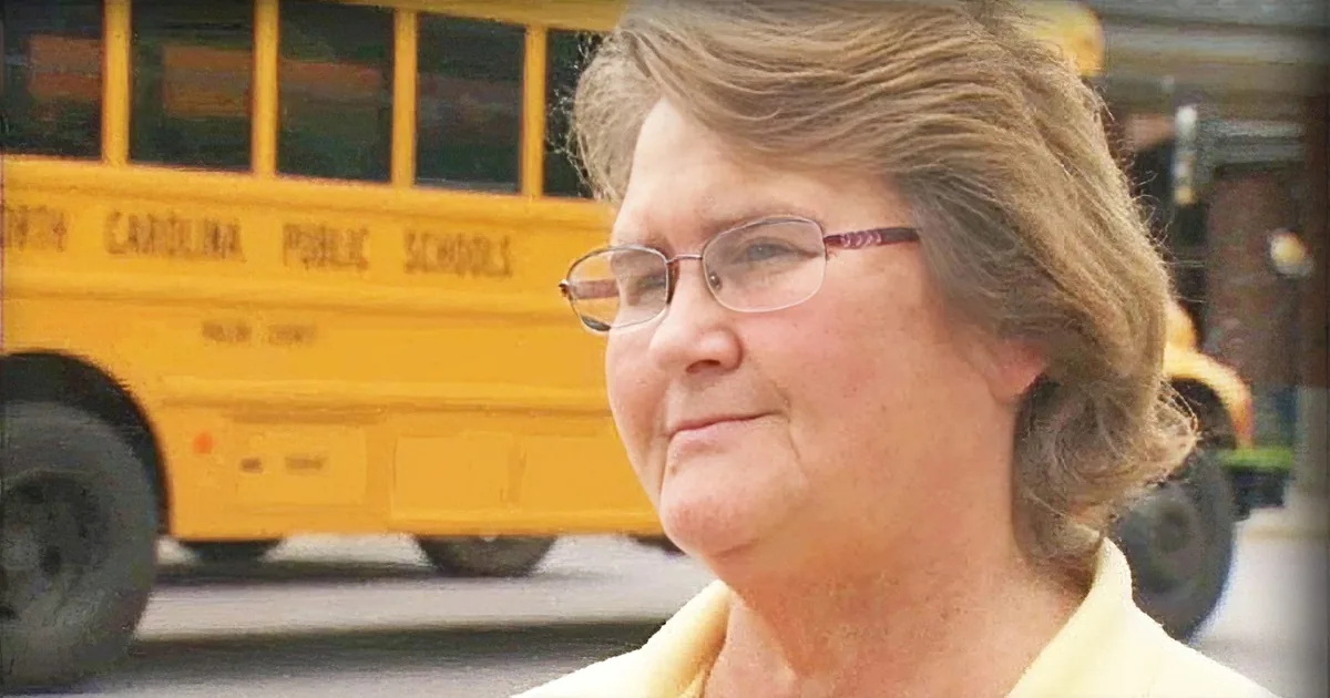 A woman with glasses and a yellow shirt stands in front of a North Carolina Public Schools bus.
