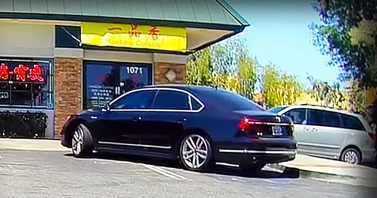 A black car is partially overlapping another car in a parking lot, creating an optical illusion.