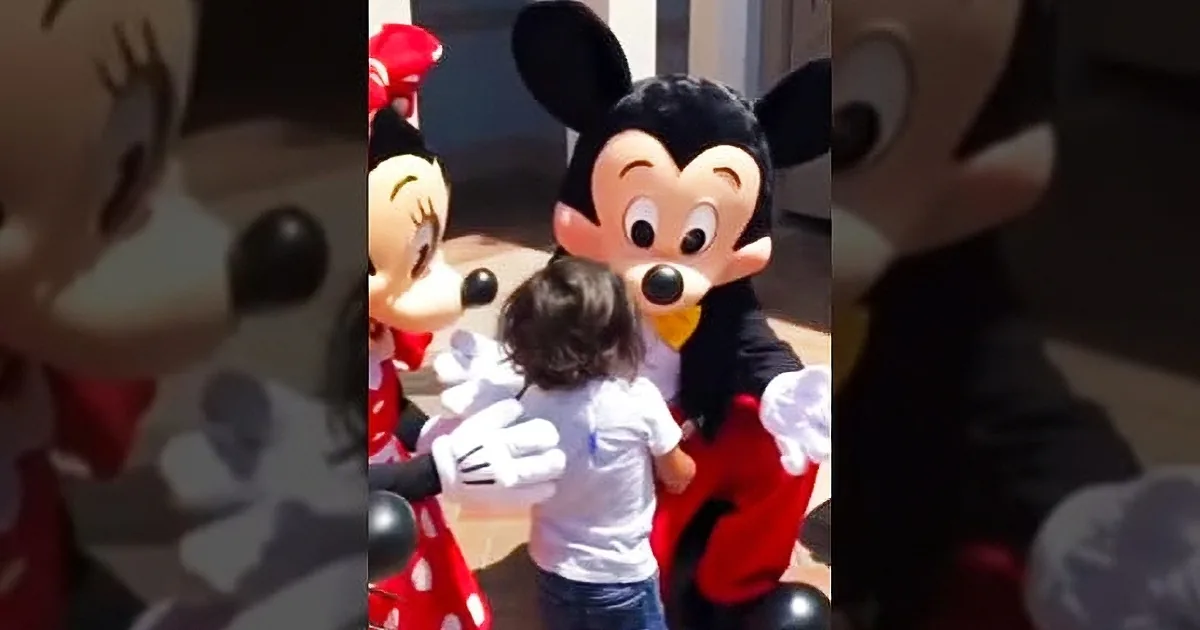 Mickey Mouse and Minnie Mouse interact with a child in a sunny outdoor setting.