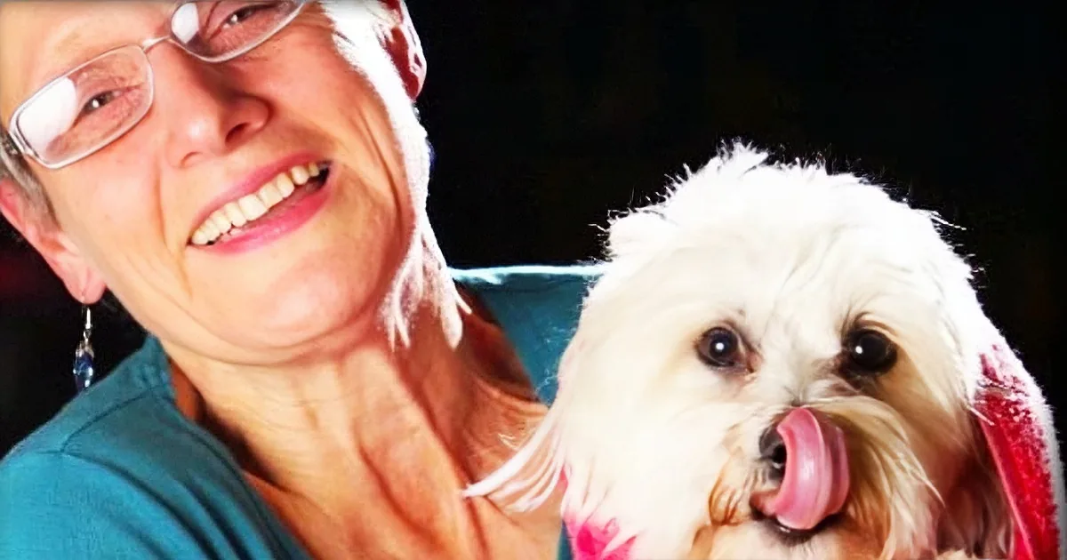 A smiling woman holds a small, fluffy white dog with a pink collar.