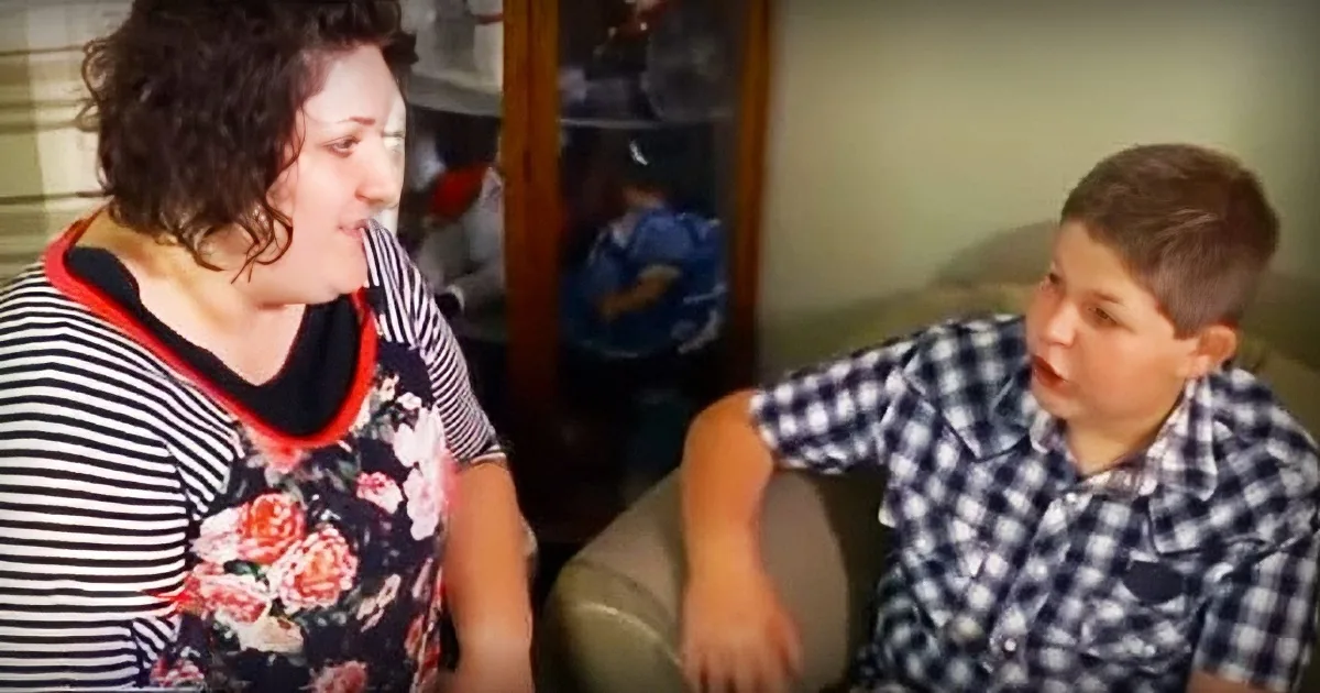 A woman in a striped shirt and floral pants is talking to a boy in a checkered shirt on a couch.