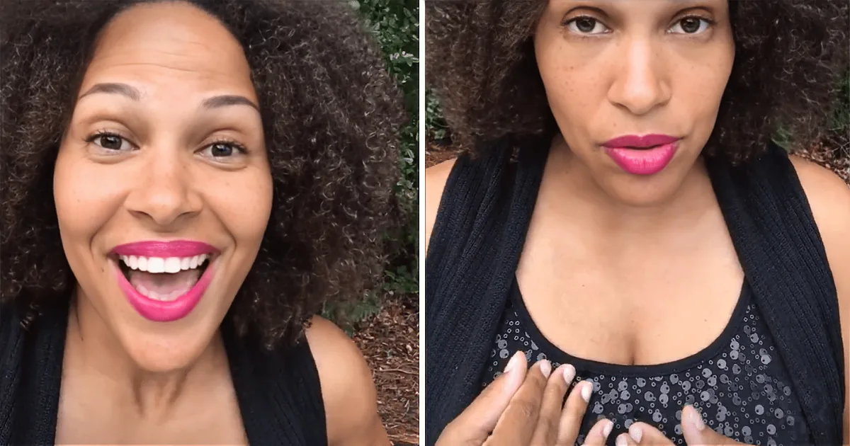 A woman with curly hair, wearing a black top, smiles and poses with her hands near her chest.