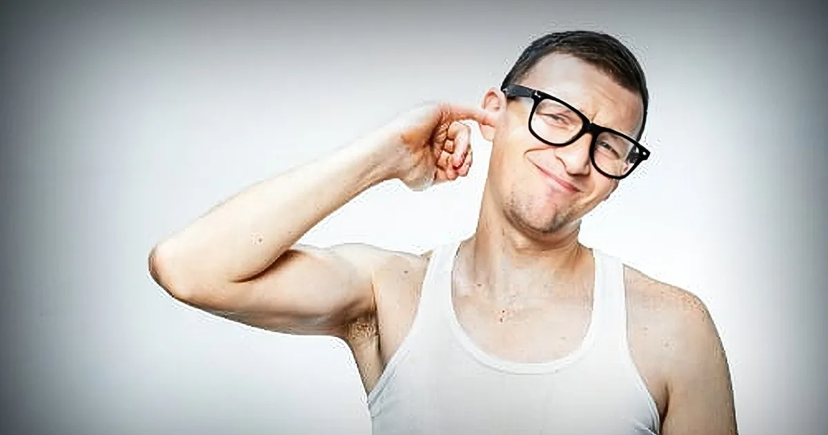 A man in a white tank top and glasses is covering his ear with his hand, looking to the side.