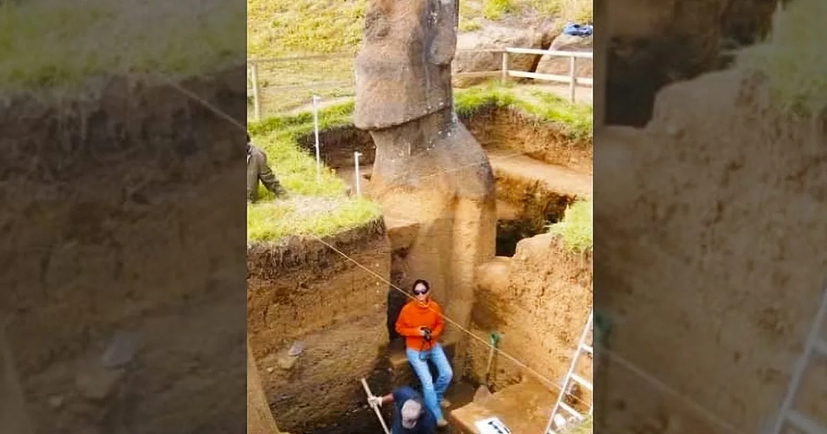 A large stone sculpture is being excavated, revealing its base, with archaeologists working around it.