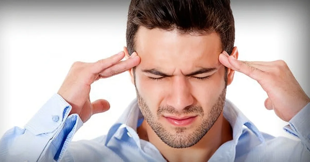 A man in a light blue shirt holds his fingers to his temples, appearing to be in thought or stress.