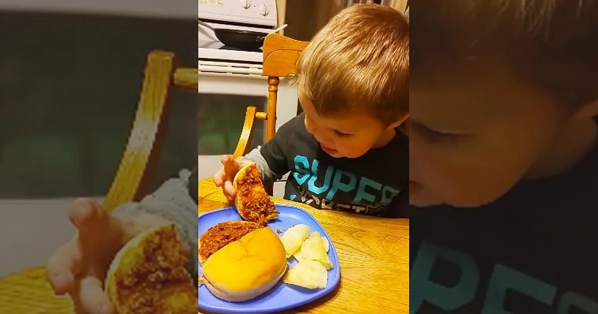 A young boy is eating a sandwich with a side of fruit on a blue plate.